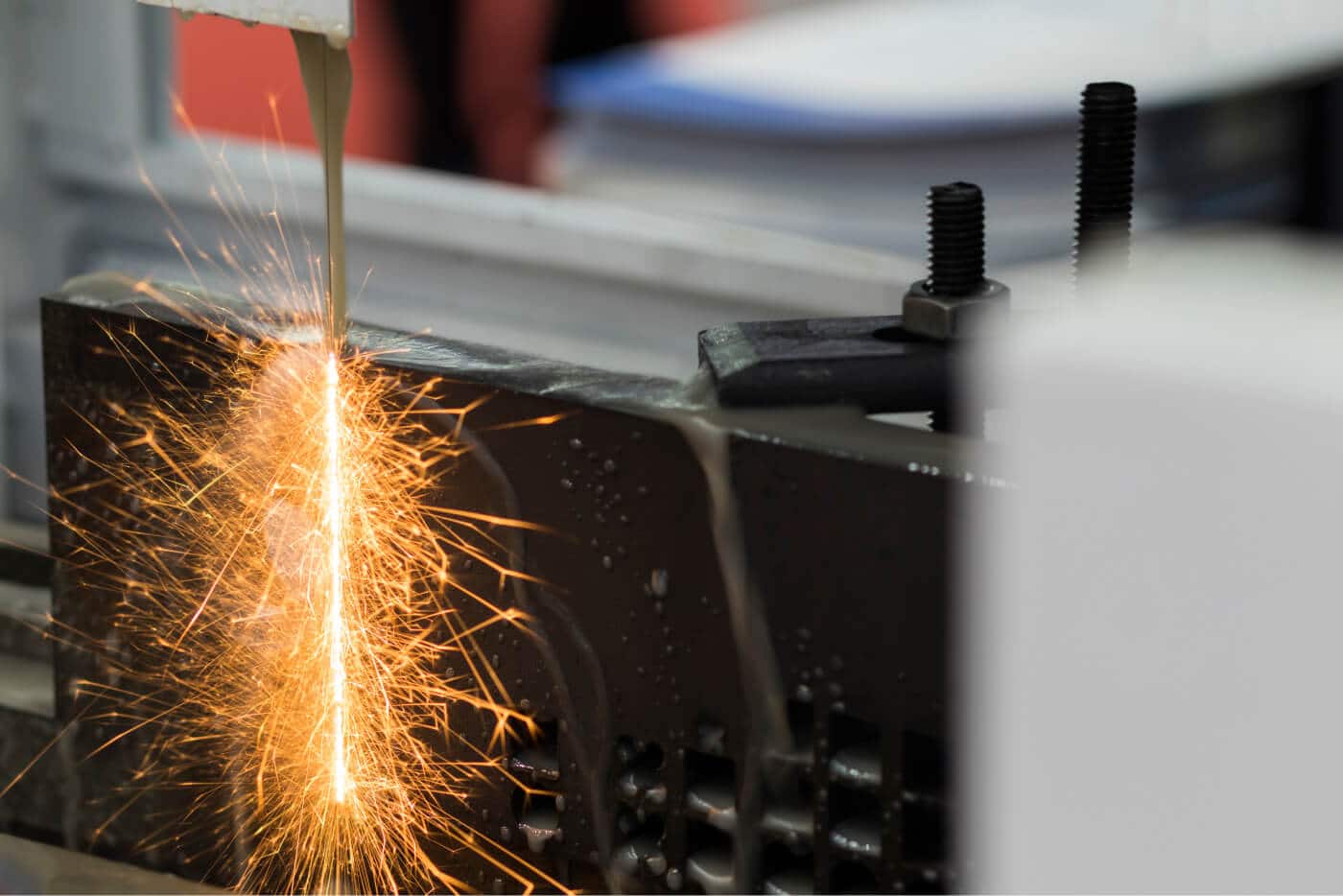 Das Bild zeigt einen Funkenerosionsprozess (EDM) an einem Metallwerkstück, bei dem Funken durch elektrische Entladung entstehen.